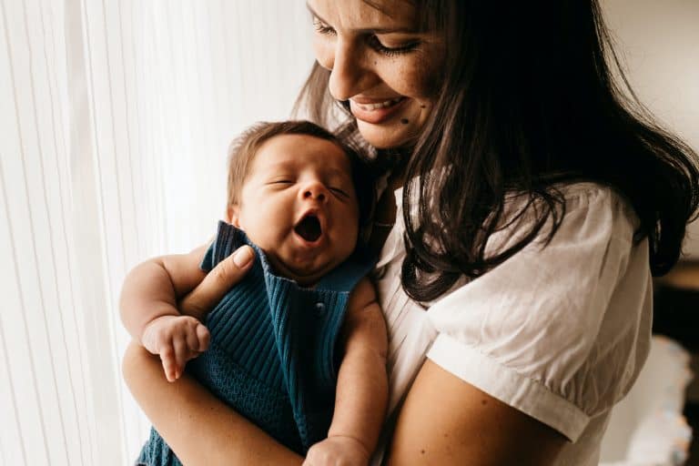 woman in white blouse holding yawning baby